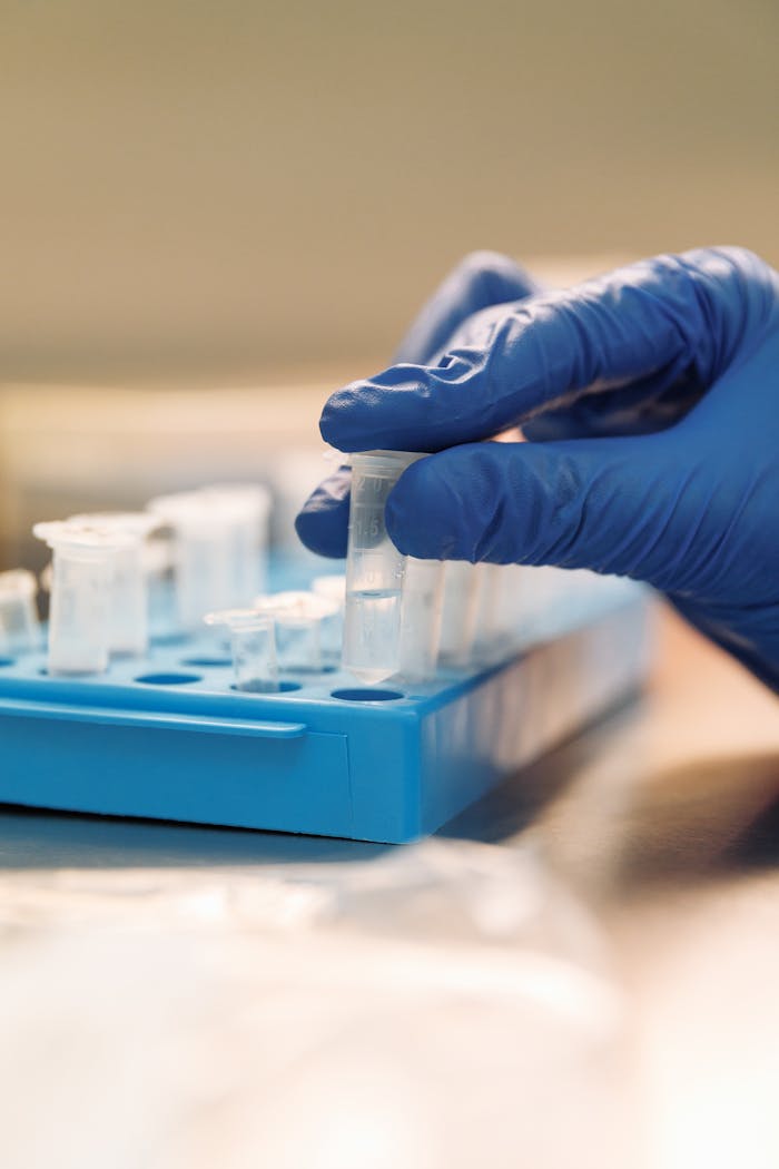 Close-up of a scientist's hand in a glove handling test tubes in a lab.